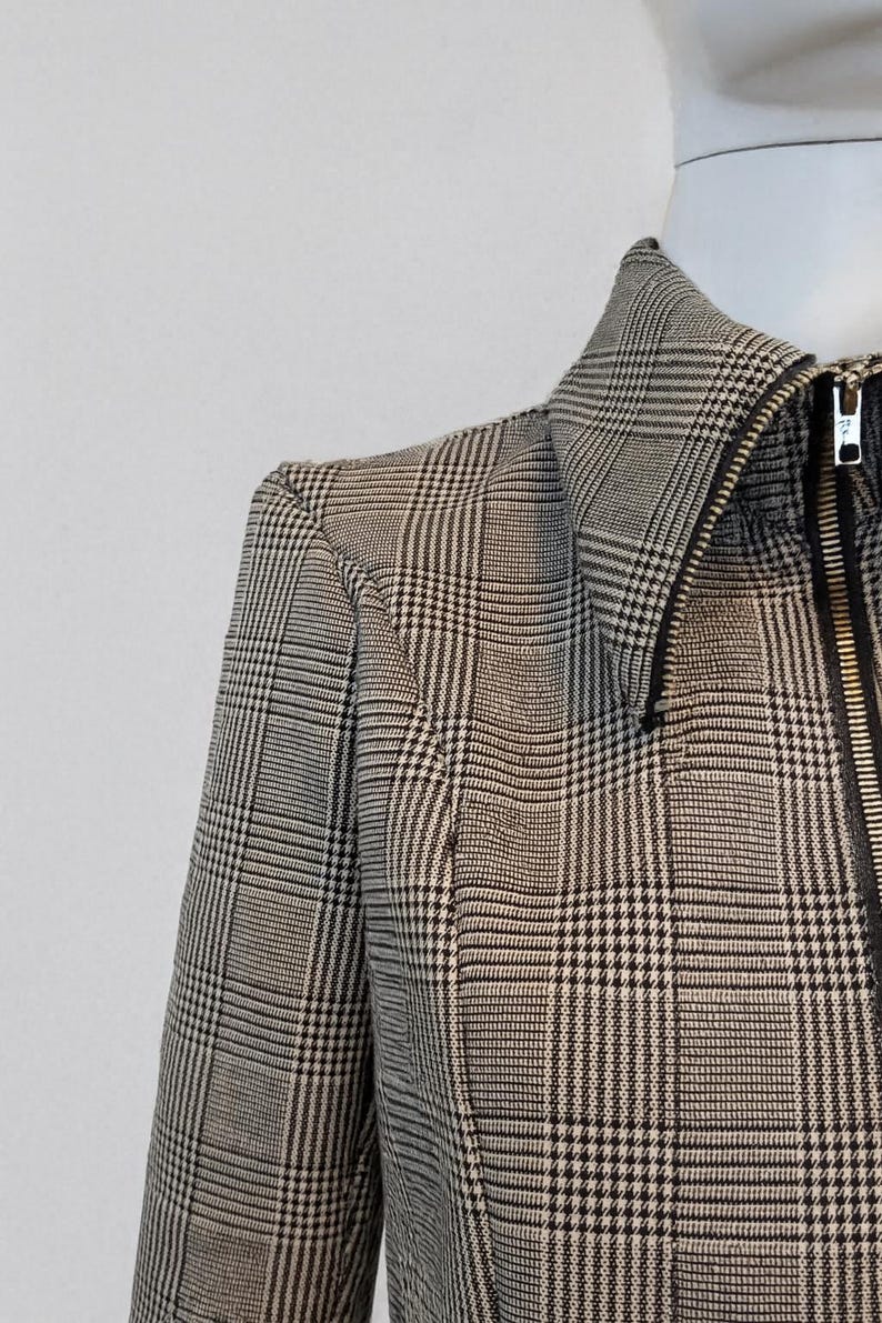 May include: Close-up of a black and white plaid jacket with a zipper closure. The jacket is displayed on a mannequin. The fabric has a classic houndstooth pattern.