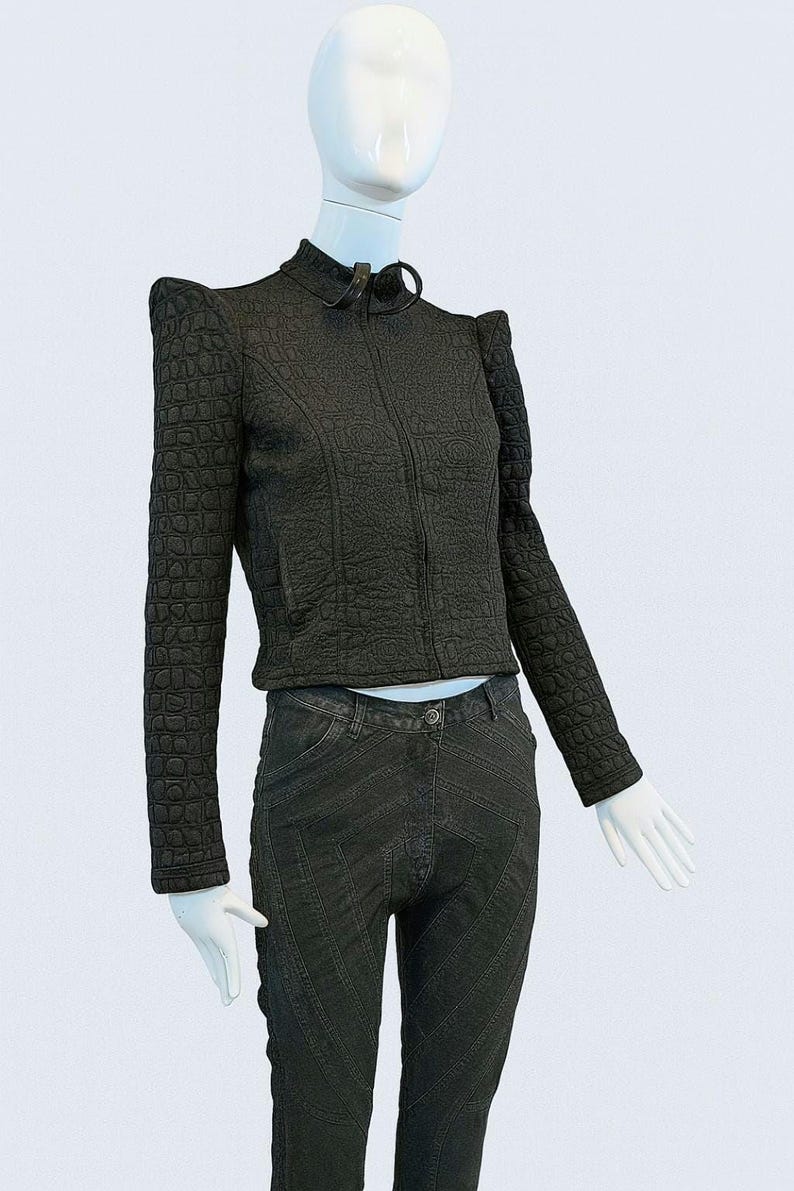 May include: A black long-sleeved jacket with a textured crocodile-skin pattern, a high collar, and a front zipper closure, paired with dark gray pants featuring prominent diagonal stitched seam detailing throughout the legs.