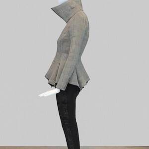 May include: A mannequin displays a stylish ensemble. The outfit features a gray and black plaid peplum jacket with a high collar, paired with black pants. The pants have a decorative design down the side. The overall look is chic and modern.