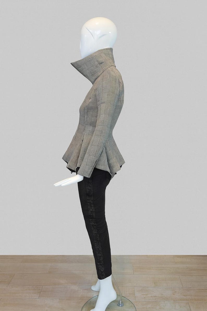 May include: A mannequin displays a stylish ensemble. The outfit features a gray and black plaid peplum jacket with a high collar, paired with black pants. The pants have a decorative design down the side. The overall look is chic and modern.