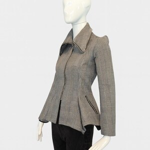 May include: A gray and black plaid jacket with a zip-up front and a flared peplum. The jacket has a wide collar and small pockets. The jacket is displayed on a mannequin.