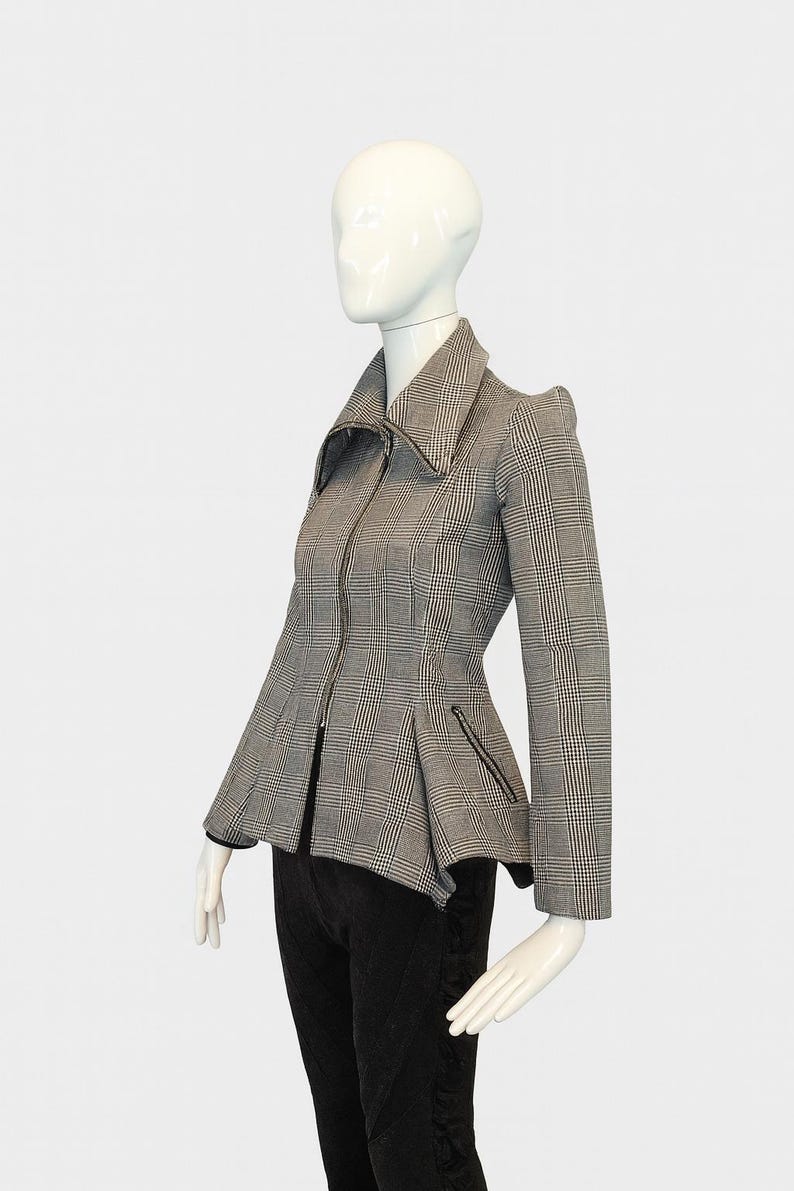 May include: A gray and black plaid jacket with a zip-up front and a flared peplum. The jacket has a wide collar and small pockets. The jacket is displayed on a mannequin.