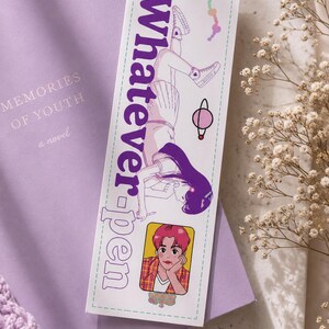 Peut inclure: Un marque-page avec le texte "Whatever-pen" et une illustration d'une personne. Il est posé sur un livre violet intitulé "Memories of Youth". L'image a une esthétique douce et pastel, avec des fleurs décoratives.