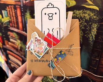 May include: A brown paper package tied with twine, containing a white card with a chicken illustration, stickers, and a pen. The package is decorated with colorful tape and the text "interactive".