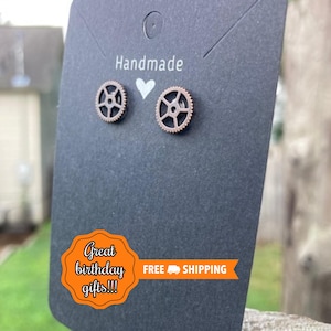 May include: A pair of bronze-colored gear-shaped stud earrings displayed on a black card. The card has the word "Handmade" printed at the top, with a white heart symbol. The earrings are presented as a great birthday gift.