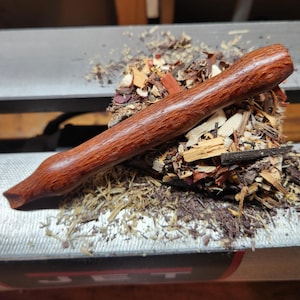May include: A handcrafted, reddish-brown wooden pipe, resting on a pile of wood shavings and sawdust. The pipe has a smooth, polished finish and a curved design. The image is taken in a workshop setting, showcasing the pipe-making process.