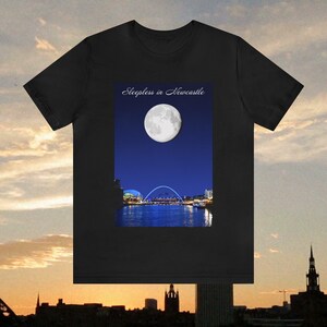May include: Black t-shirt featuring a nighttime scene with a full moon over a city skyline and a bridge. The text "Sleepless in Newcastle" is printed above the image. The shirt is made of a soft material.