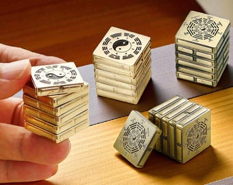 May include: Several gold-colored, stackable, square blocks with intricate black designs, including Yin and Yang symbols. Some blocks are stacked, while others are separate. The blocks are on a wooden surface.