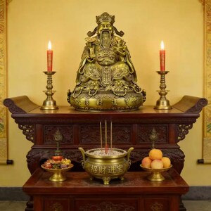 May include: A traditional Asian altar with a golden deity statue as the focal point. Lit red candles in brass holders sit either side of the statue. Incense and offerings are displayed on the lower level, with the text "招财进宝" on a golden incense burner.