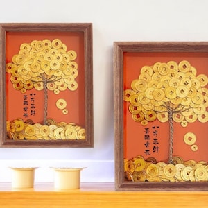 Puede incluir: Dos obras de arte enmarcadas representan un árbol hecho de monedas de oro sobre un fondo naranja. El tronco y las ramas del árbol son de alambre, y los marcos son de color marrón oscuro. La obra incluye caracteres chinos.