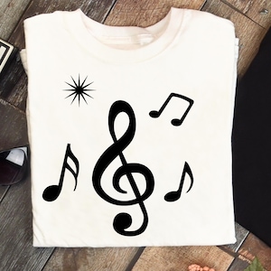 May include: White t-shirt featuring a black treble clef, musical notes, and a starburst design. The graphic is centered on the shirt, creating a simple yet stylish design. The shirt is made of a soft material.