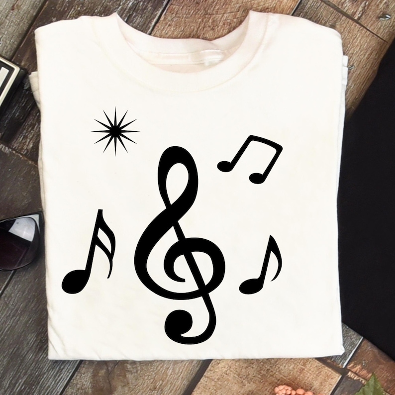 May include: White t-shirt featuring a black treble clef, musical notes, and a starburst design. The graphic is centered on the shirt, creating a simple yet stylish design. The shirt is made of a soft material.