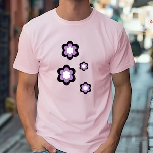 May include: A pale pink t-shirt with a floral pattern. The flowers have black outlines, purple petals, and white centres. The design is repeated in different sizes across the shirt. The t-shirt is short-sleeved.