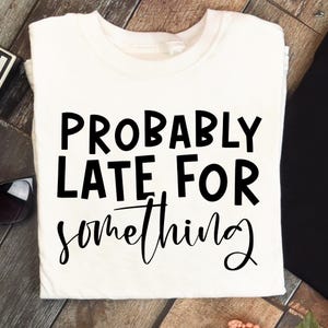 K&ouml;nnte beinhalten: Ein wei&szlig;es T-Shirt mit dem schwarzen Aufdruck "PROBABLY LATE FOR something". Der Text ist fett gedruckt, das Wort "something" ist kursiv geschrieben. Das T-Shirt ist gefaltet.
