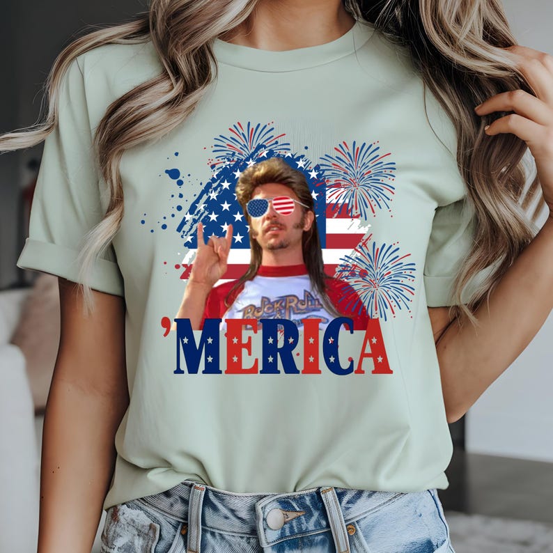 Op de afbeelding: Lichtgroen t-shirt met een afbeelding van een man met een zonnebril en een hanenkam, met het woord 'MERICA in rood, wit en blauw. Het ontwerp bevat een Amerikaanse vlag en vuurwerk.