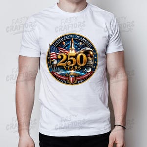 K&ouml;nnte beinhalten: Ein wei&szlig;es T-Shirt mit einem kreisf&ouml;rmigen Motiv und dem Text United States of America 250 Years 1776-2026. Das Design zeigt ein Space Shuttle, einen Astronautenhelm, eine amerikanische Flagge, einen Wei&szlig;kopfseeadler und ein Wappenschild.