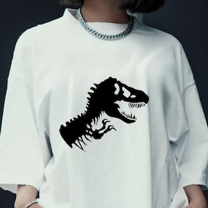 May include: White t-shirt featuring a black dinosaur graphic. The graphic is a stylized silhouette of a Tyrannosaurus Rex head and upper body. The shirt has a crew neck and short sleeves, and is made of a soft, comfortable material.