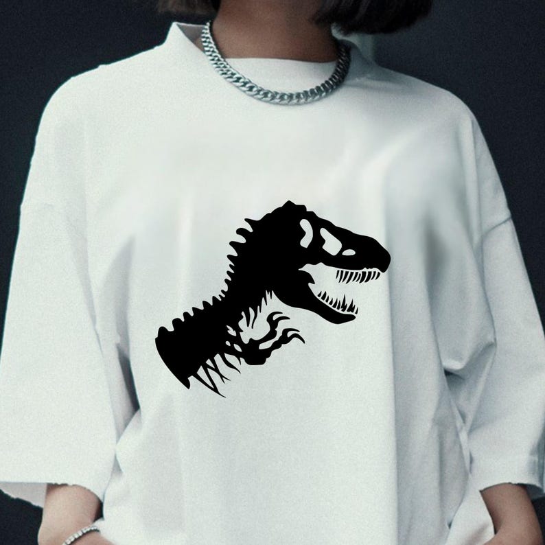 May include: White t-shirt featuring a black dinosaur graphic. The graphic is a stylized silhouette of a Tyrannosaurus Rex head and upper body. The shirt has a crew neck and short sleeves, and is made of a soft, comfortable material.