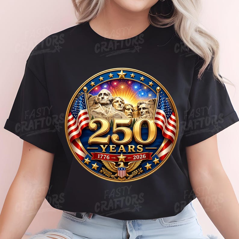 K&ouml;nnte beinhalten: Ein schwarzes T-Shirt mit einer kreisf&ouml;rmigen Grafik, die den Mount Rushmore, zwei amerikanische Flaggen und einen goldenen Adler zeigt. Der Text lautet 250 YEARS, 1776 und 2026. Das Design umfasst einen sternf&ouml;rmigen Rahmen und Feuerwerk.