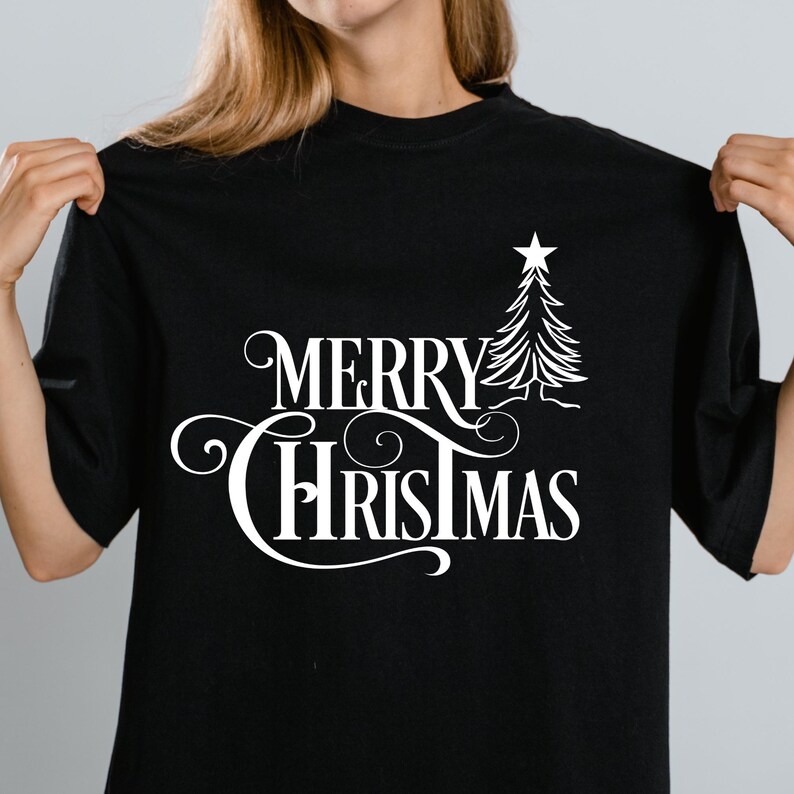 May include: Black t-shirt with the white text "MERRY CHRISTMAS" in a decorative font, accompanied by a stylized Christmas tree and star. The shirt is a casual style, suitable for holiday celebrations.