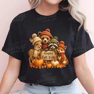 May include: A black t-shirt featuring a graphic of a fawn, bear cub, raccoon, and fox wearing knit hats and scarves. They are gathered around a wooden sign that reads Happy Fall Y'all, with orange pumpkins and autumn leaves at their feet.