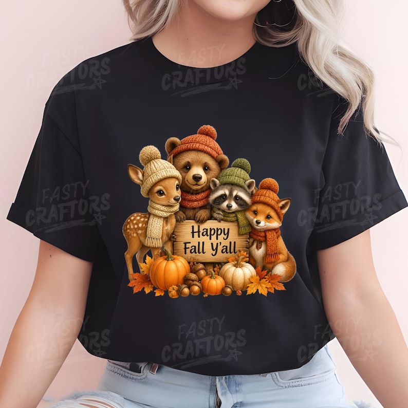 May include: A black t-shirt featuring a graphic of a fawn, bear cub, raccoon, and fox wearing knit hats and scarves. They are gathered around a wooden sign that reads Happy Fall Y'all, with orange pumpkins and autumn leaves at their feet.