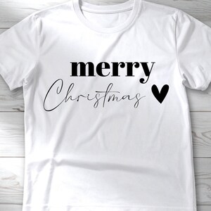 May include: White t-shirt with the words "merry Christmas" in black, with a black heart symbol. The word "merry" is in a bold, sans-serif font, while "Christmas" is in a cursive script.
