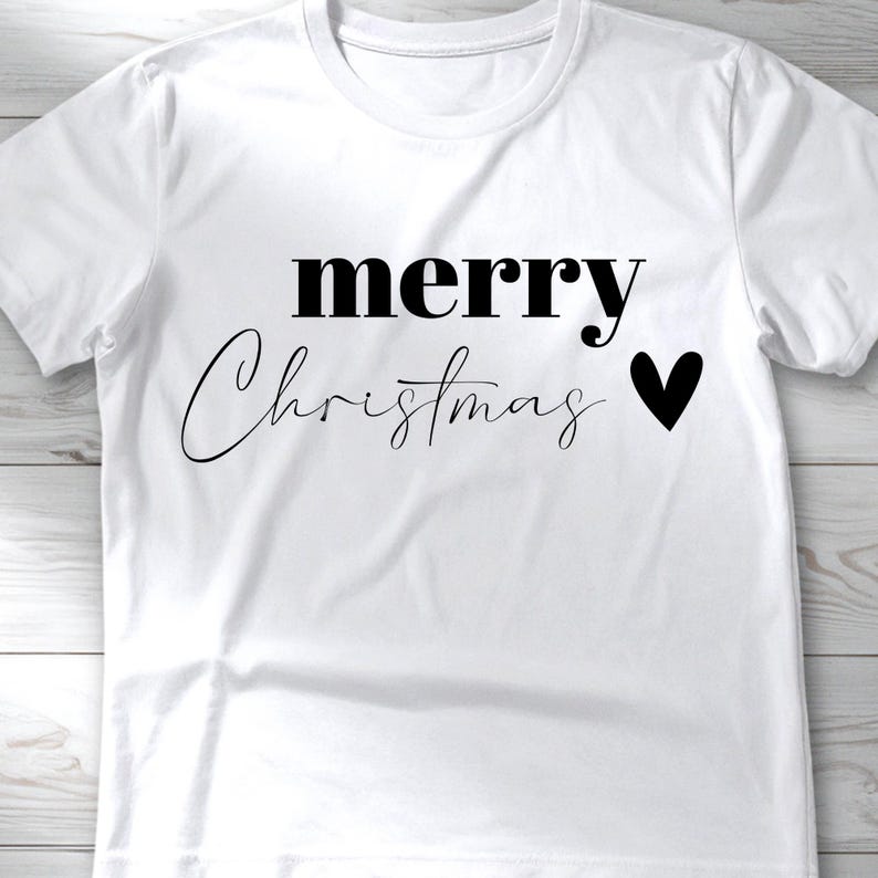 May include: White t-shirt with the words "merry Christmas" in black, with a black heart symbol. The word "merry" is in a bold, sans-serif font, while "Christmas" is in a cursive script.