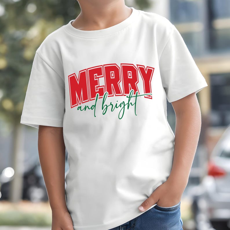 Puede incluir: Camiseta blanca con las palabras "MERRY and bright" en letras rojas y verdes. La palabra "MERRY" est&aacute; en una fuente en negrita y en bloque, mientras que "and bright" est&aacute; en cursiva.
