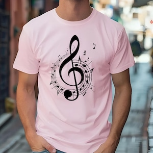 May include: A light pink t-shirt featuring a black treble clef design surrounded by musical notes. The musical notes are arranged in a circular pattern around the clef. The shirt is a short-sleeved crew neck.