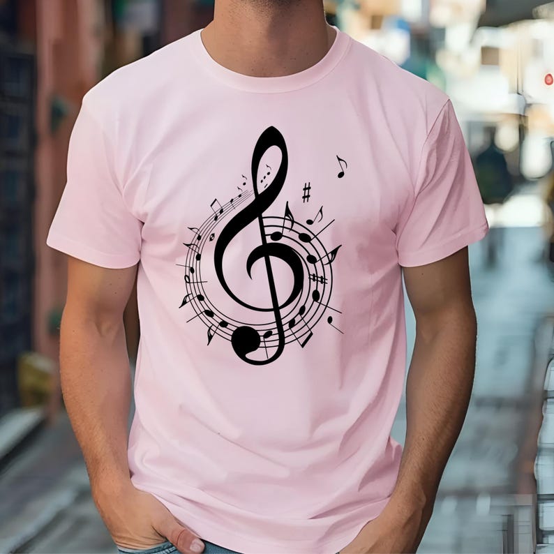 May include: A light pink t-shirt featuring a black treble clef design surrounded by musical notes. The musical notes are arranged in a circular pattern around the clef. The shirt is a short-sleeved crew neck.