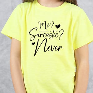 K&ouml;nnte beinhalten: Hellgelbes T-Shirt mit dem schwarzen Schriftzug "Me? Sarcastic? Never". Das Design enth&auml;lt zwei kleine schwarze Herzen. Das T-Shirt hat einen Rundhalsausschnitt und kurze &Auml;rmel.
