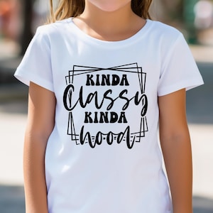 K&ouml;nnte beinhalten: Wei&szlig;es T-Shirt mit dem Text "Kinda Classy Kinda Hood" in schwarzer, fetter Schrift. Der Text ist in einem schwarzen geometrischen Rahmen eingeschlossen. Das Shirt hat kurze &Auml;rmel und einen Rundhalsausschnitt.