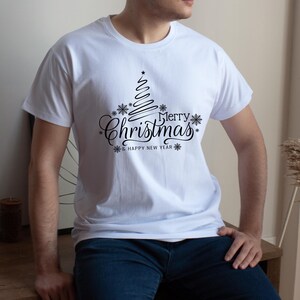 May include: White t-shirt with a black Christmas tree design and the words "Merry Christmas & Happy New Year". The design includes snowflakes and a star at the top of the tree. The shirt is a crew neck.