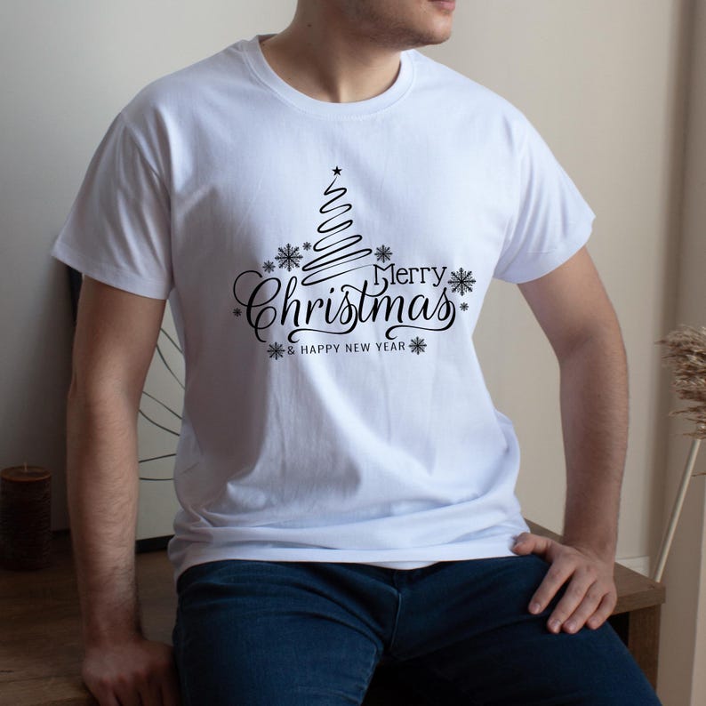 May include: White t-shirt with a black Christmas tree design and the words "Merry Christmas & Happy New Year". The design includes snowflakes and a star at the top of the tree. The shirt is a crew neck.