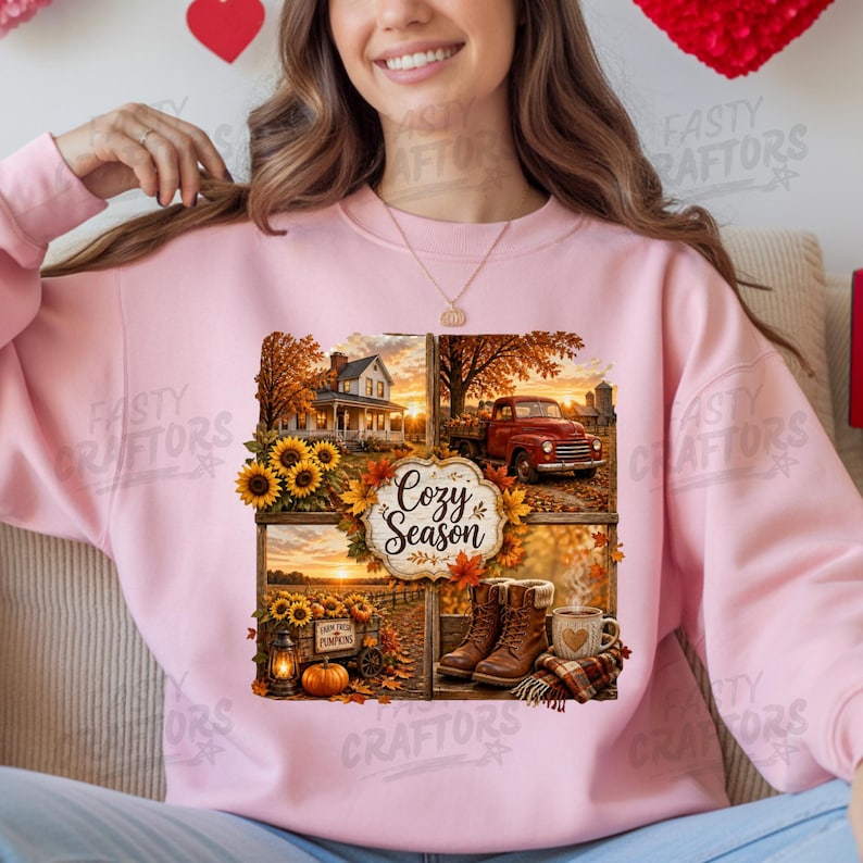 May include: A light pink crewneck sweatshirt featuring a multi-panel graphic print. The design displays a farmhouse, a red truck, sunflowers, a pumpkin, boots, and a mug with the text Cozy Season surrounded by autumn leaves and golden light.