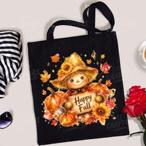 May include: A black tote bag featuring a graphic of a scarecrow wearing a straw hat, surrounded by orange pumpkins, yellow sunflowers, and autumn leaves. The scarecrow holds a wooden sign with the text Happy Fall printed in brown letters.