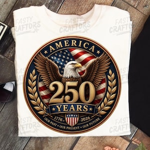 K&ouml;nnte beinhalten: Ein wei&szlig;es T-Shirt mit einer kreisf&ouml;rmigen Grafik, die einen Wei&szlig;kopfseeadler, die amerikanische Flagge und den Text AMERICA 250 YEARS zeigt. Das Design enth&auml;lt die Jahreszahlen 1776 und 2026, ein kleines Schild und den Schriftzug OUR PAST OUR PRESENT OUR FUTURE.