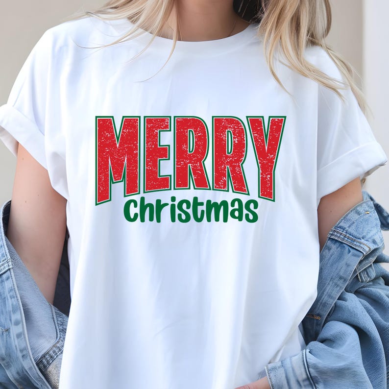Puede incluir: Camiseta blanca con la frase "MERRY Christmas" en rojo, con contorno verde. El texto tiene un aspecto desgastado. Prenda casual y festiva para Navidad.