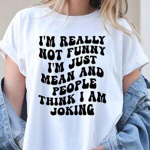 K&ouml;nnte beinhalten: Wei&szlig;es T-Shirt mit dem schwarzen Text: "I'M REALLY NOT FUNNY I'M JUST MEAN AND PEOPLE THINK I AM JOKING." Das Shirt hat kurze &Auml;rmel und eine lockere Passform. Der Text ist fett und abgerundet.