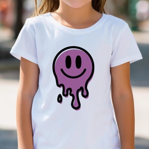 May include: White t-shirt with a purple melting smiley face design outlined in black. The graphic has two black oval eyes and a curved smile. The design is centered on the front of the shirt.