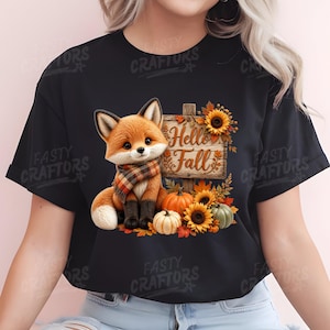 May include: A black t-shirt featuring a graphic of a fox wearing a plaid scarf, sitting next to a wooden sign that reads Hello Fall. The design includes orange and white pumpkins, sunflowers, and autumn leaves surrounding the fox and sign.