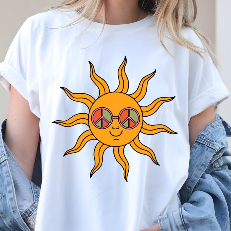 May include: White t-shirt with a cartoon sun design. The sun has orange rays, a smiling face, and wears round glasses with peace signs. The design is centrally placed, giving a retro and cheerful appearance.