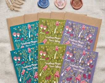May include: An assortment of greeting cards with mushroom and floral illustrations, alongside wax seals in various colors. The cards feature the text "Sending Magic Your Way" and come with brown envelopes.