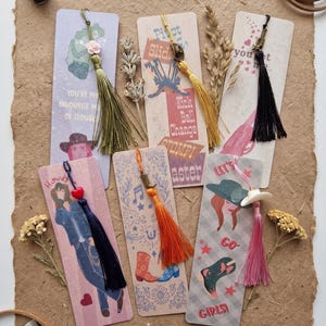 Puede incluir: Una colección de marcapáginas hechos a mano con varios diseños y detalles de borlas. Los marcapáginas presentan ilustraciones de vaqueros, botas y frases como "Howdy" y "Girls!" en un tema rústico y campestre. Cada marcapáginas tiene una combinación de colores única.