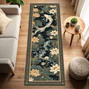 May include: A rectangular rug with a dark blue background featuring a koi carp, lotus flowers, and lily pads. The rug has a beige border with a geometric pattern. The design incorporates shades of white, beige, and green.