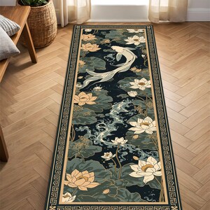 May include: A rectangular rug featuring a koi carp swimming amongst lotus flowers. The rug has a dark blue background with cream and green accents. A cream border with a geometric pattern frames the design.