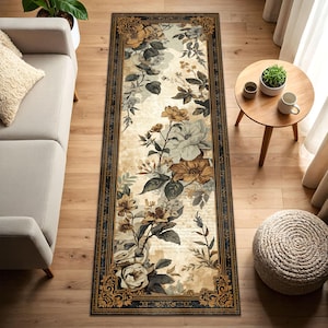 May include: A rectangular floral rug with a cream background and a black border. The rug features a pattern of roses and other flowers in shades of brown, cream, and grey. The rug is placed on a wooden floor.