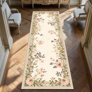 Puede incluir: Una alfombra de pasillo rectangular con motivos florales, fondo crema y borde de flores rosas, verdes y moradas. La alfombra está colocada sobre un suelo de madera, y el diseño incluye rosas y otros elementos florales.