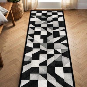 May include: Geometric patterned runner rug in black, white, and grey. The rug features a repeating pattern of squares, triangles, and other shapes. The rug has a black border and is placed on a wooden floor.